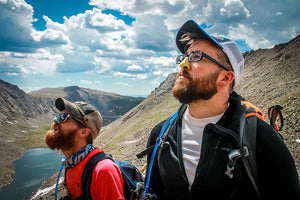 Two men hiking with colorful Nöz sunscreen on their noses. 